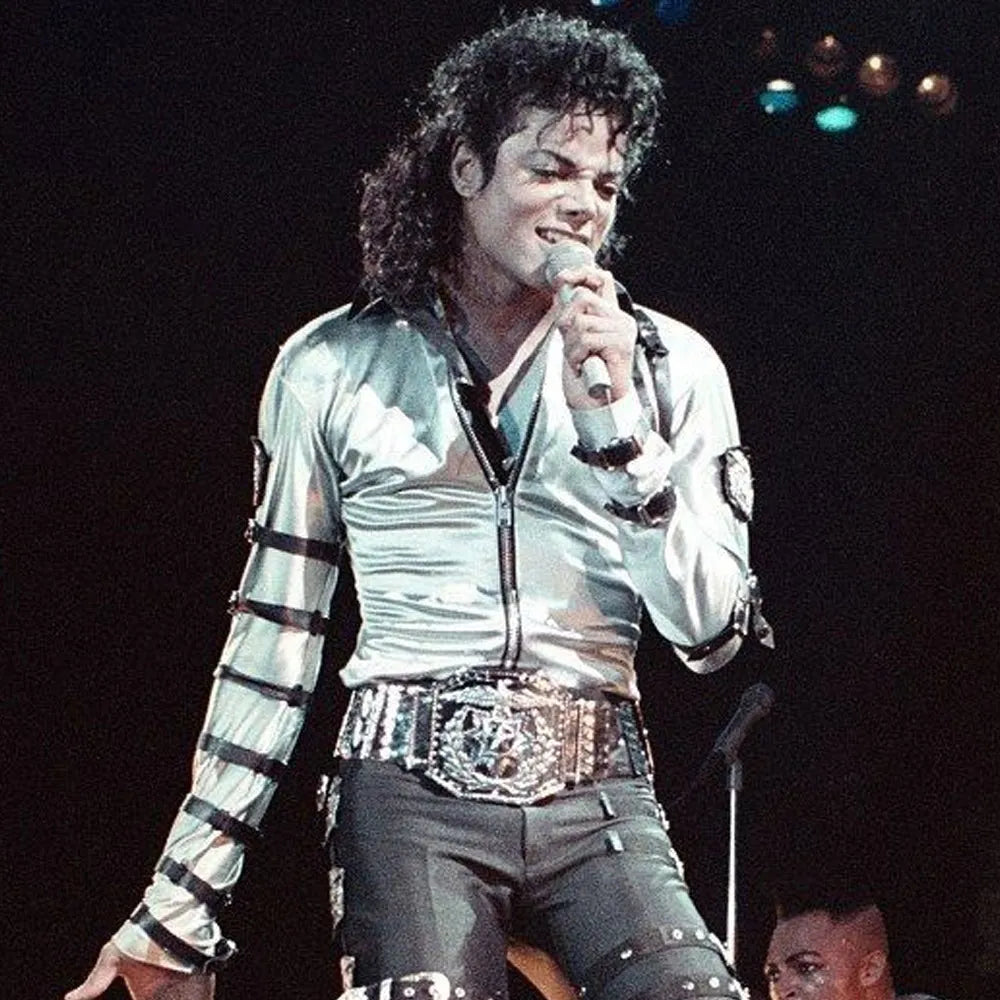 Person in a silver jacket with reflective material on stage holding a microphone.