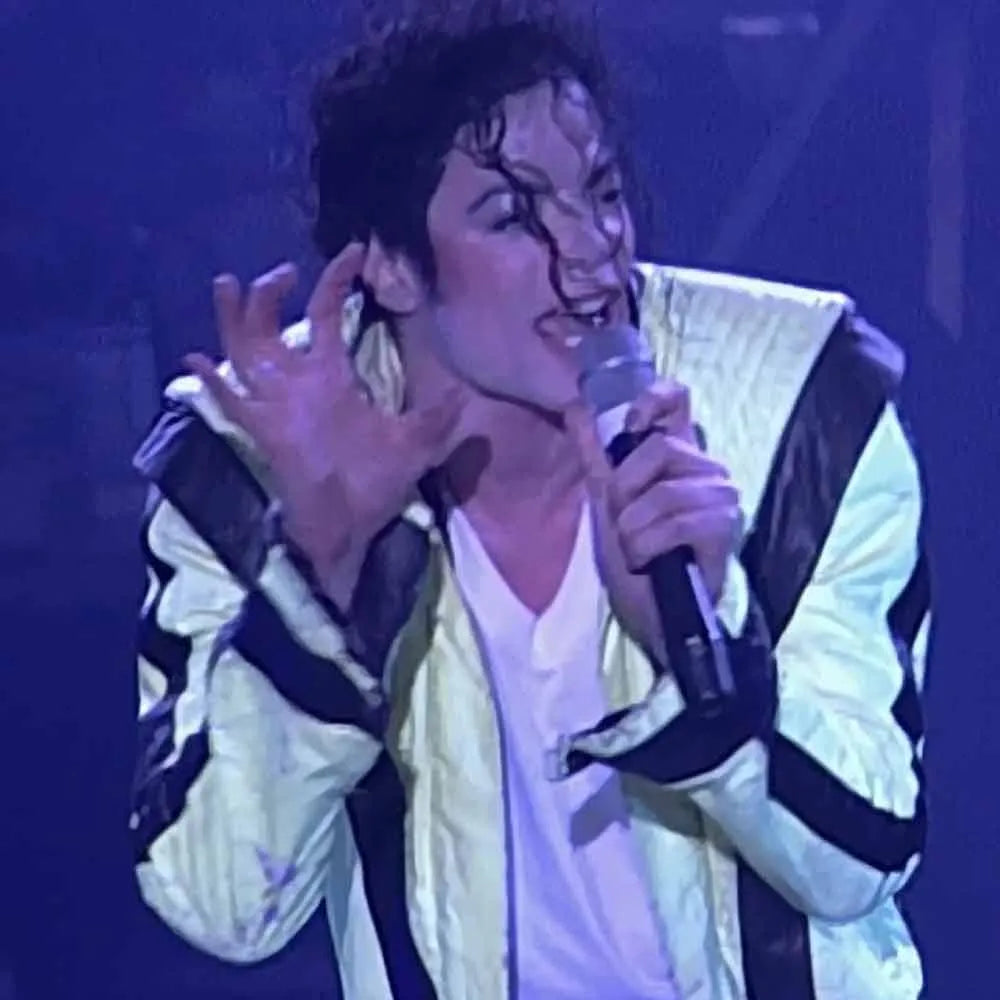 Person in a white and black jacket holding a microphone on a stage with blue lighting