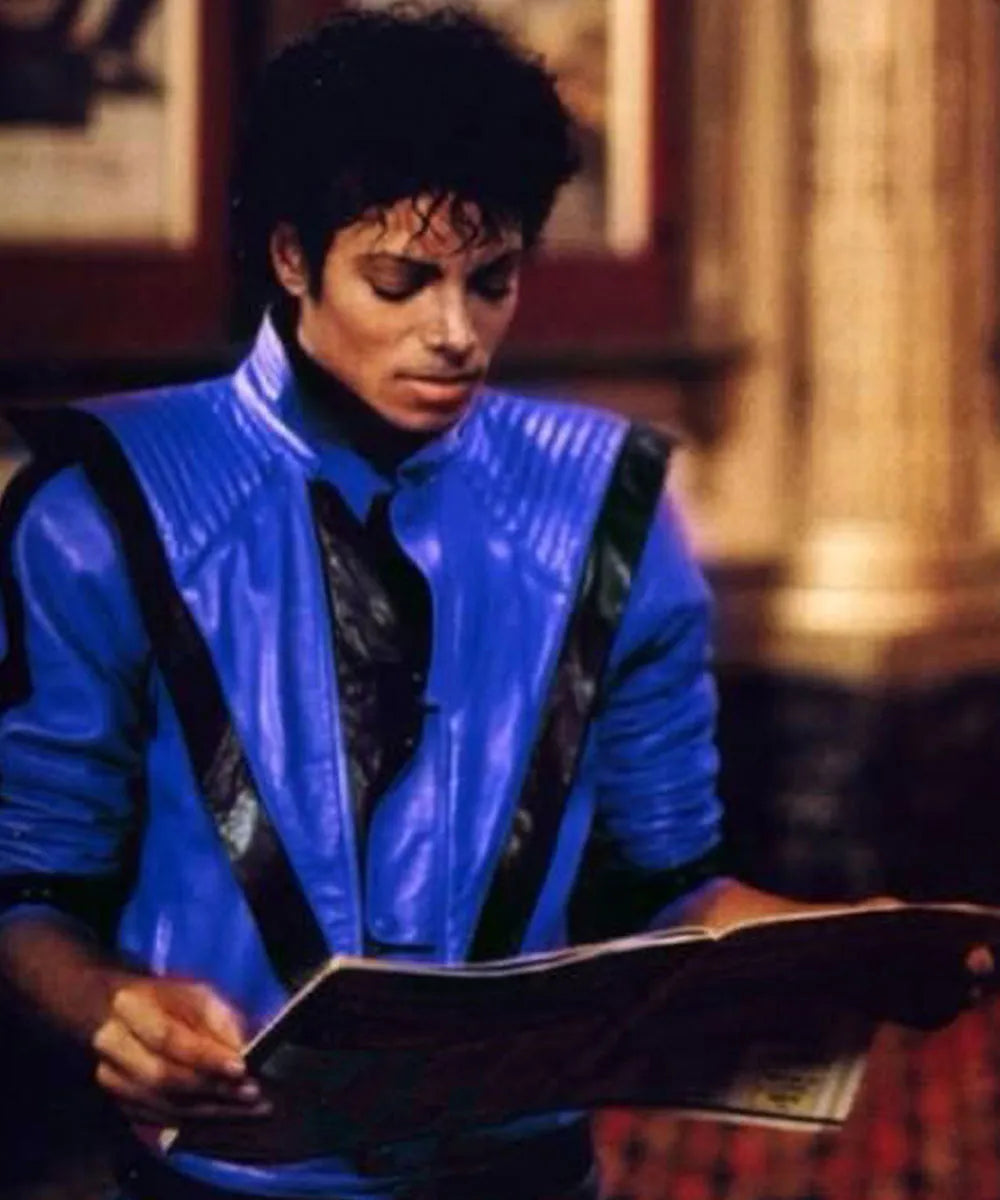 Person wearing a blue jacket with a guitar, holding a book in an indoor setting