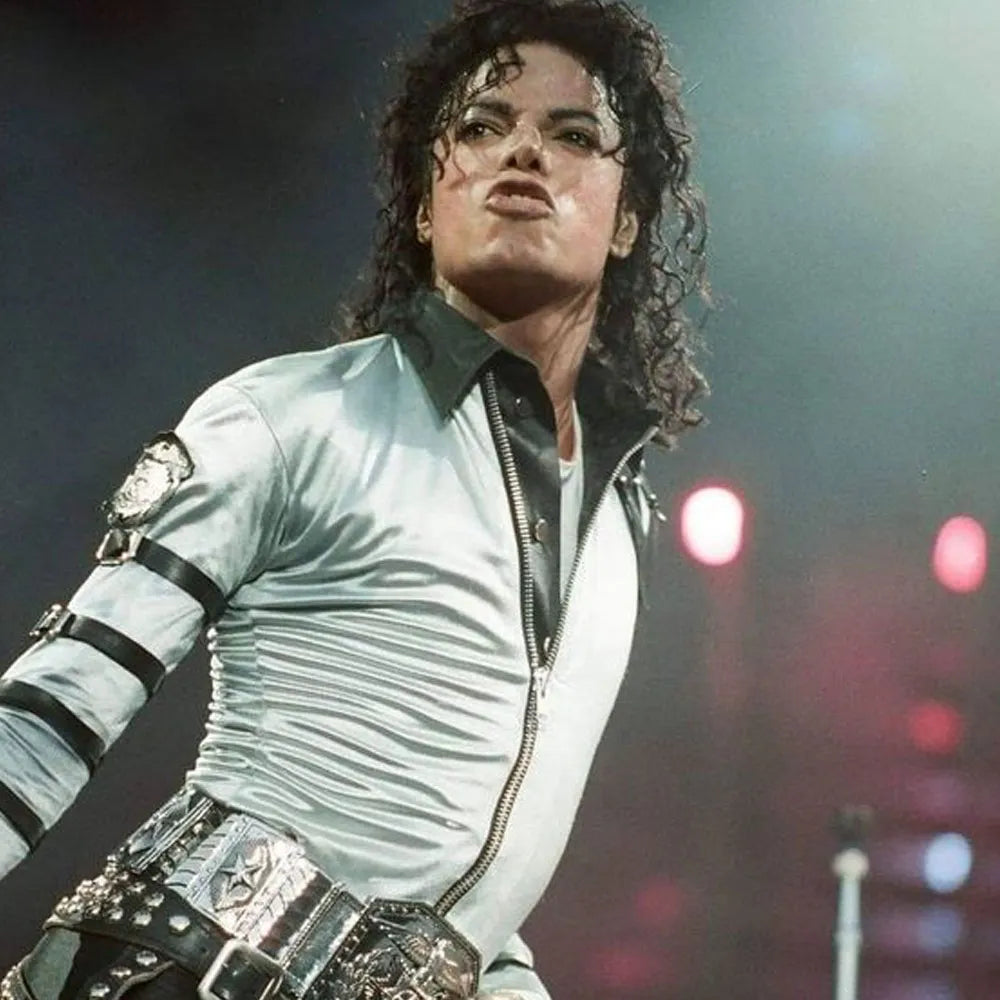 Person wearing a light-colored jacket with dark accents on a stage with blurred lights in the background