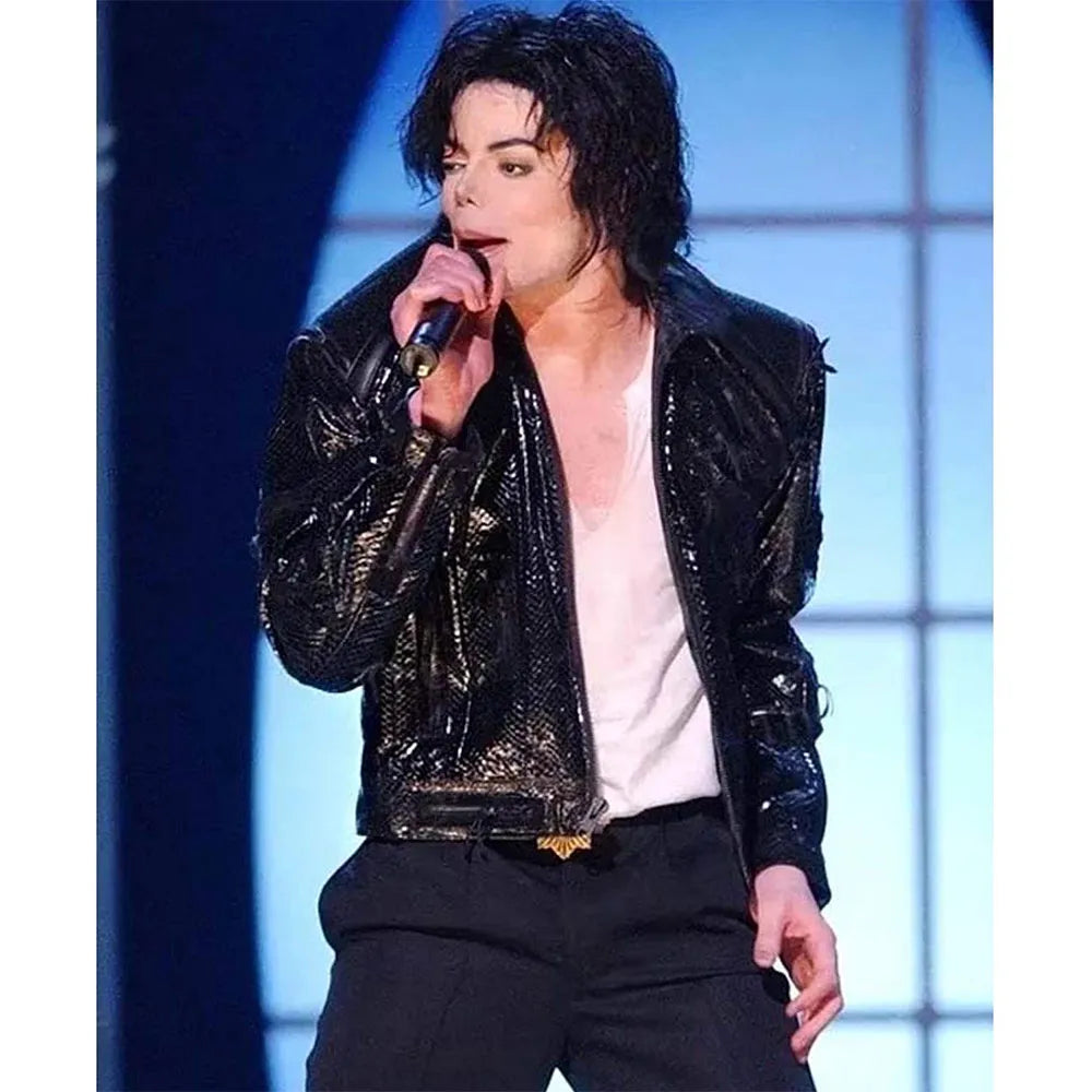 Person wearing a shiny black jacket on stage with a microphone