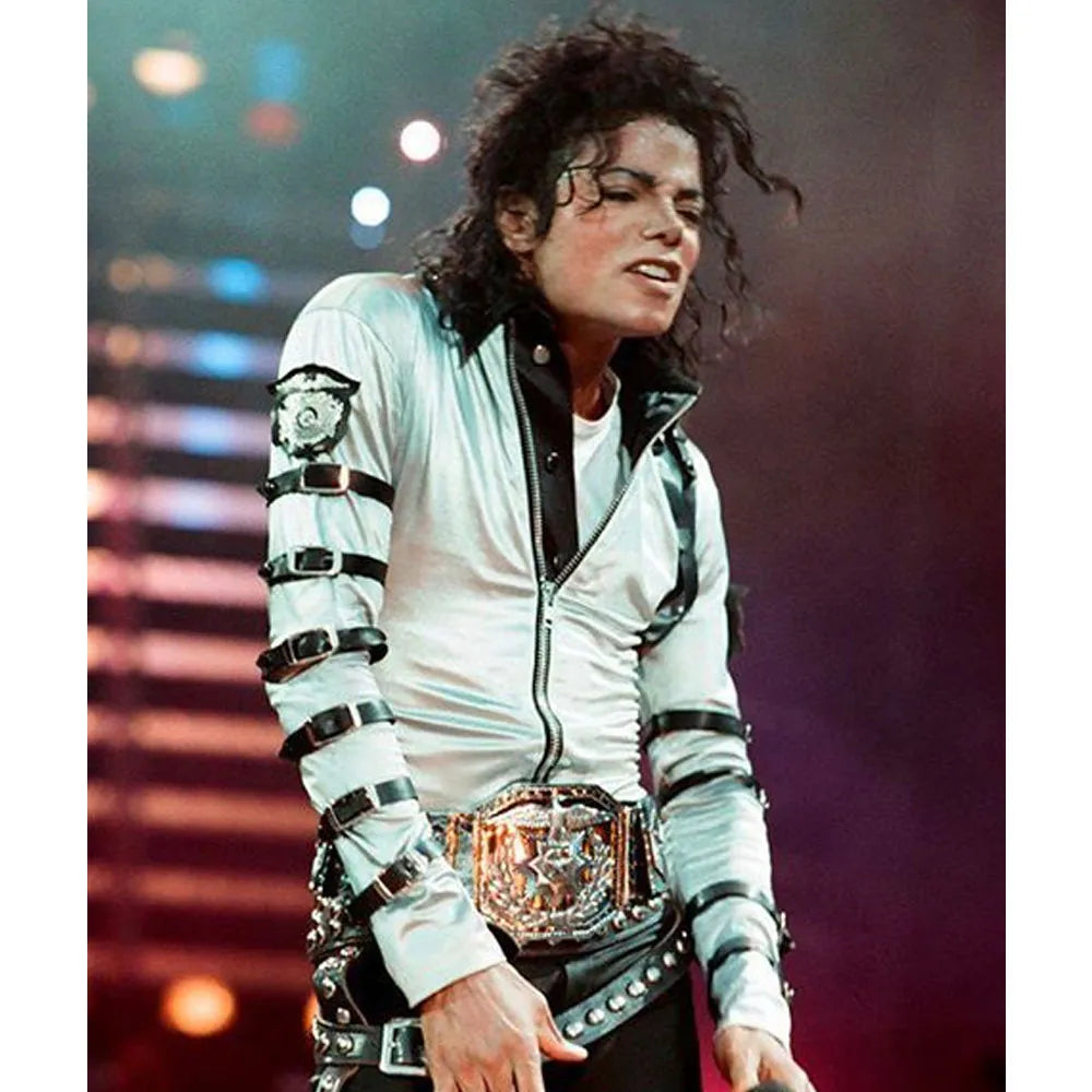 Person wearing a white jacket with black accents and a belt buckle, standing on a stage with colorful lights in the background.